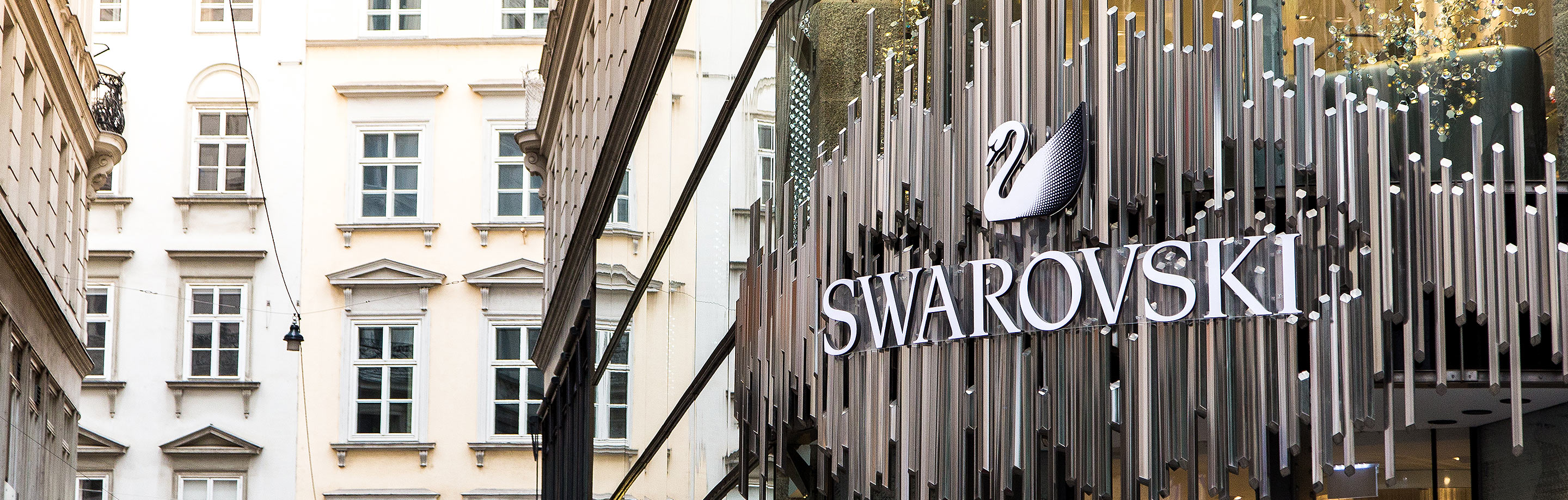 Außenansicht eines Swarovski Stores mit Logo und Schwan-Symbol vor historischen Altbau-Fassaden