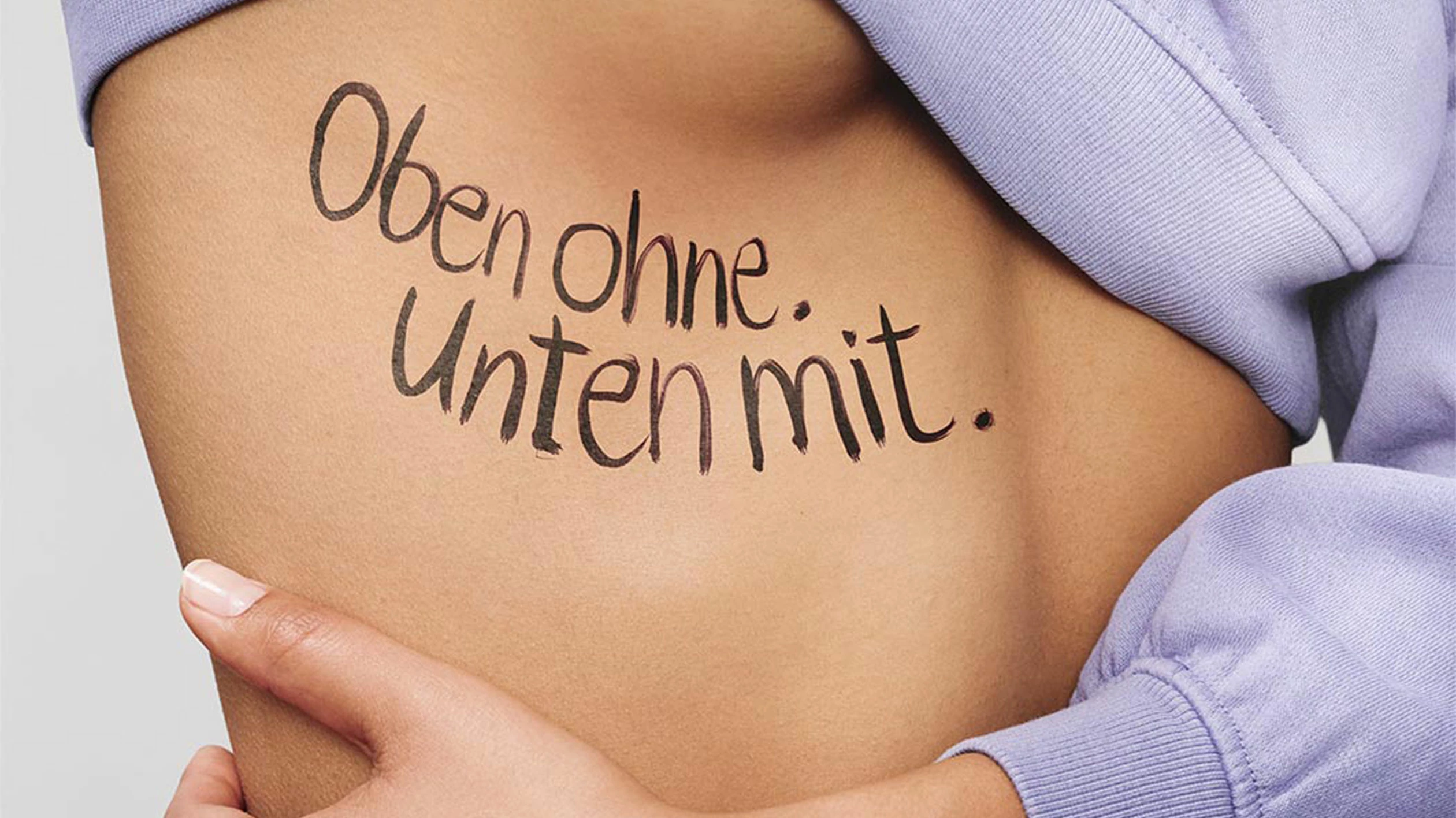 A female upper body is covered with a sweater up to chest height. Her skin can be seen in the stomach area, on which the slogan Oben ohne. Unten mit” is written in black.