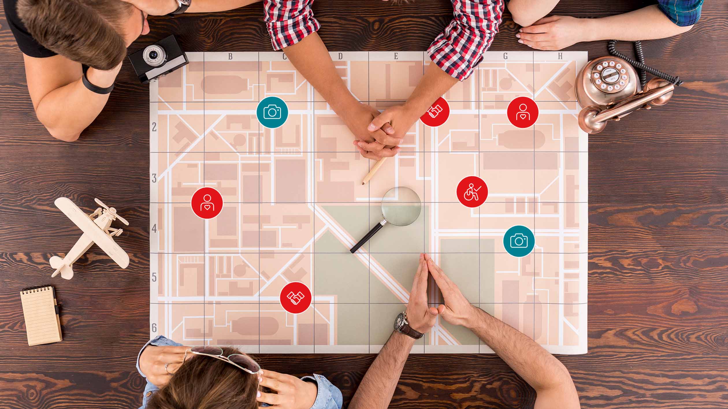 View from above of a table at which several people are sitting: On the table is a large, abstract road map