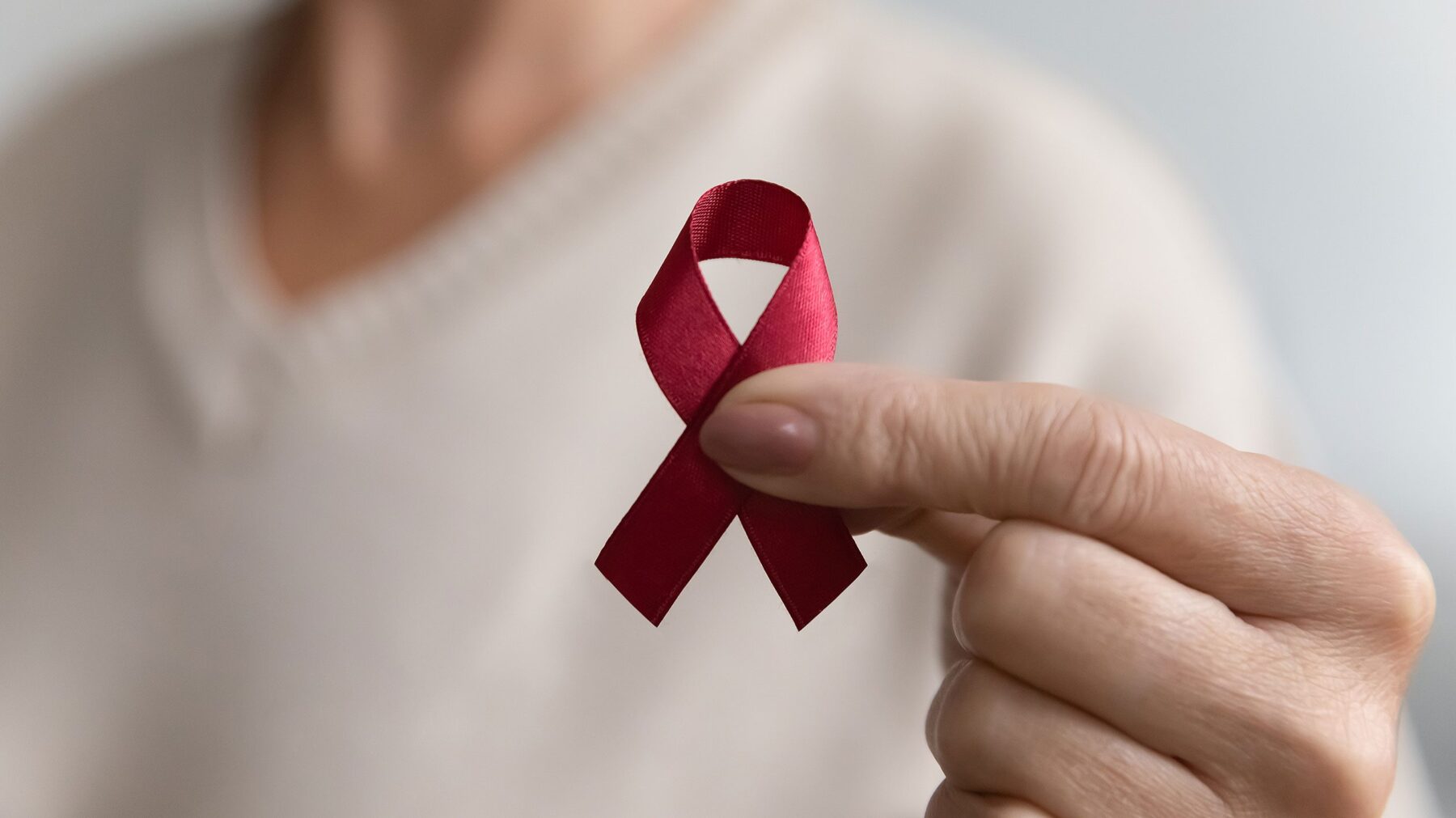 One thumb and one index finger hold a red AIDS ribbon.