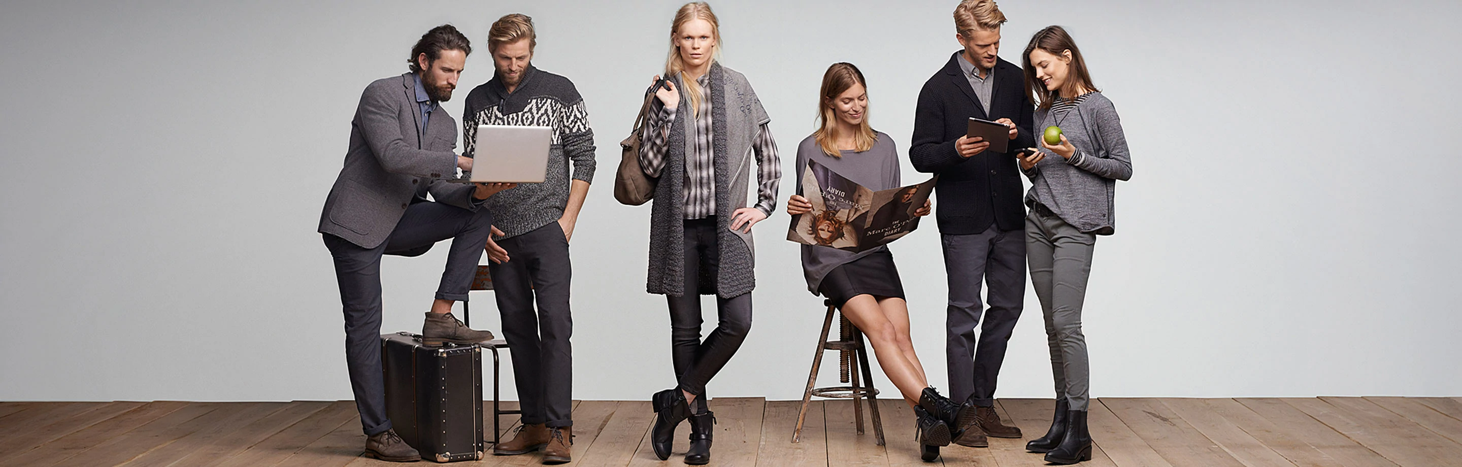 A group photo with three female and three male models in a studio. Some of the people are looking at a laptop and tablet, reading a Marc'O'Polo magazine or looking towards the camera.