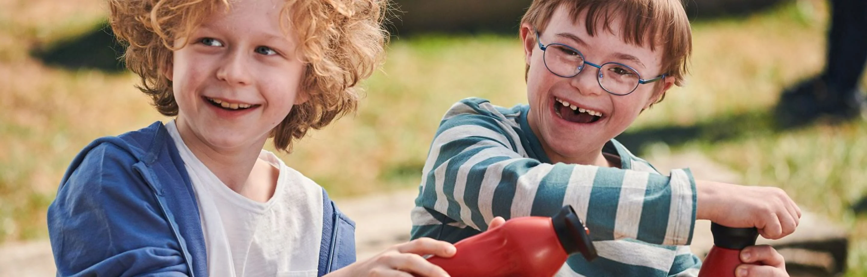 Zwei lachende Jungen im Grundschulalter mit Trinkflaschen auf einem Spielplatz