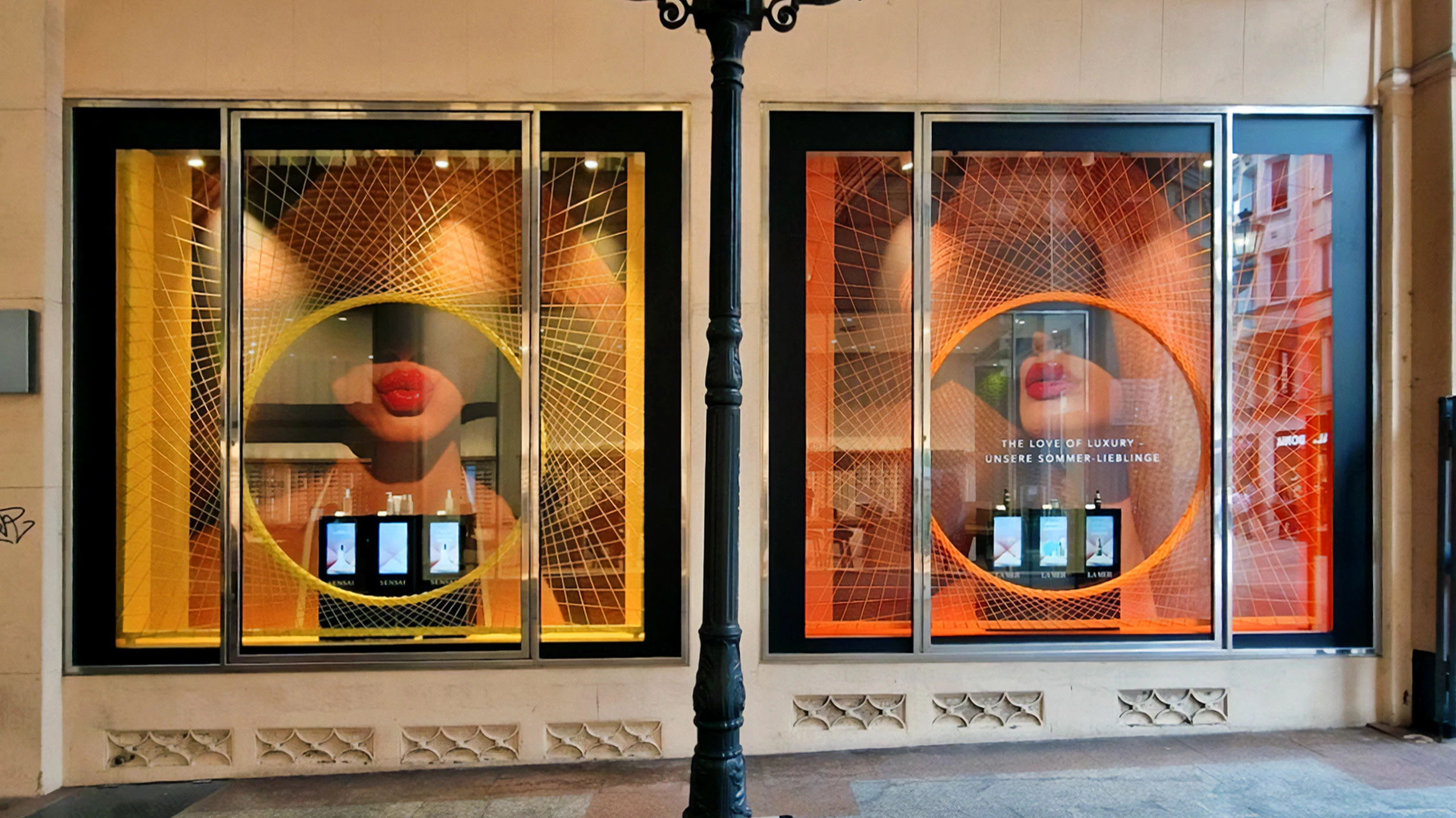 Shop window of a Douglas store in which threads in neon colors are stretched over a large area. Products are placed on a counter in the middle of the shop window. 