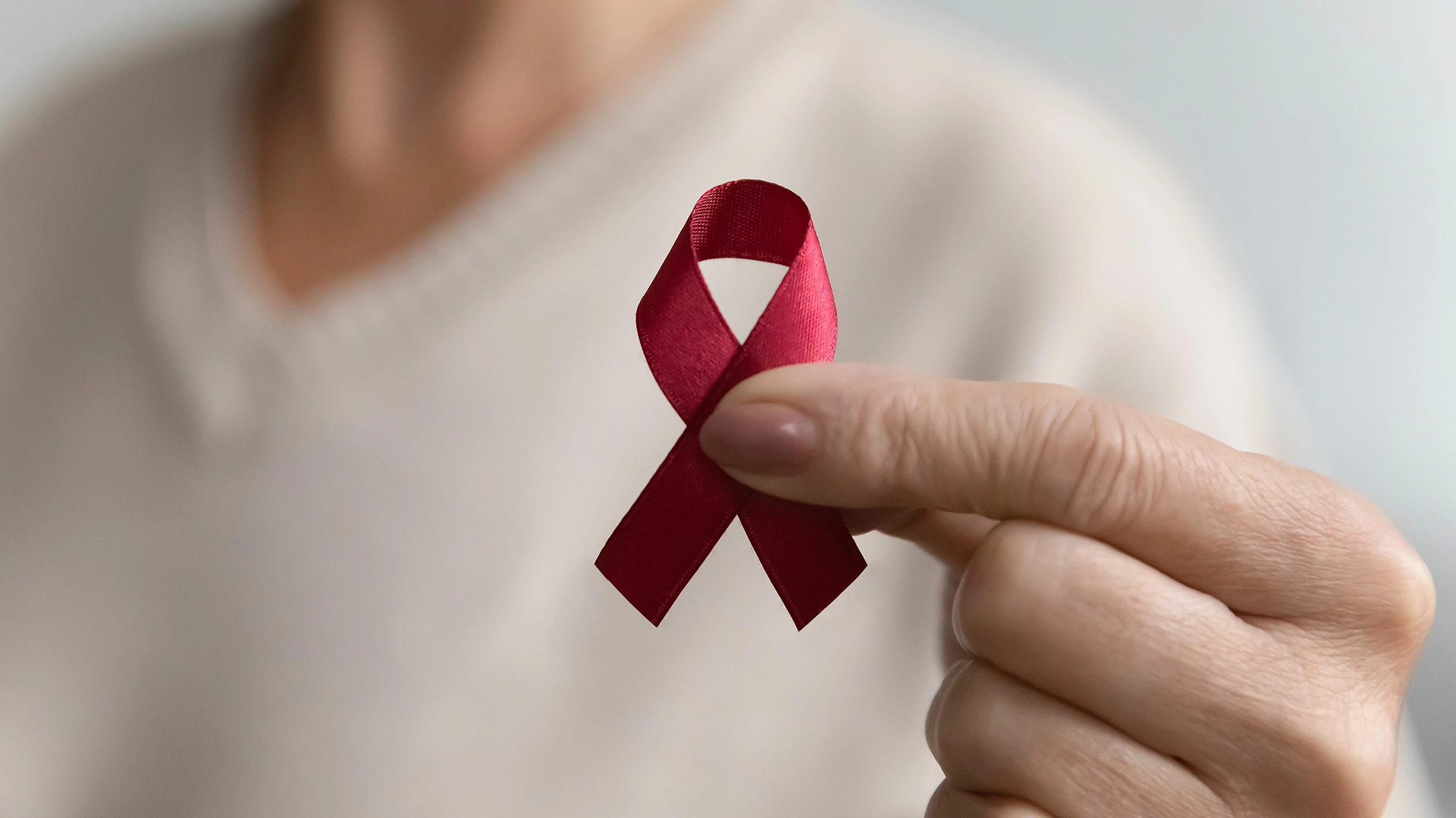 One thumb and one index finger hold a red AIDS ribbon.