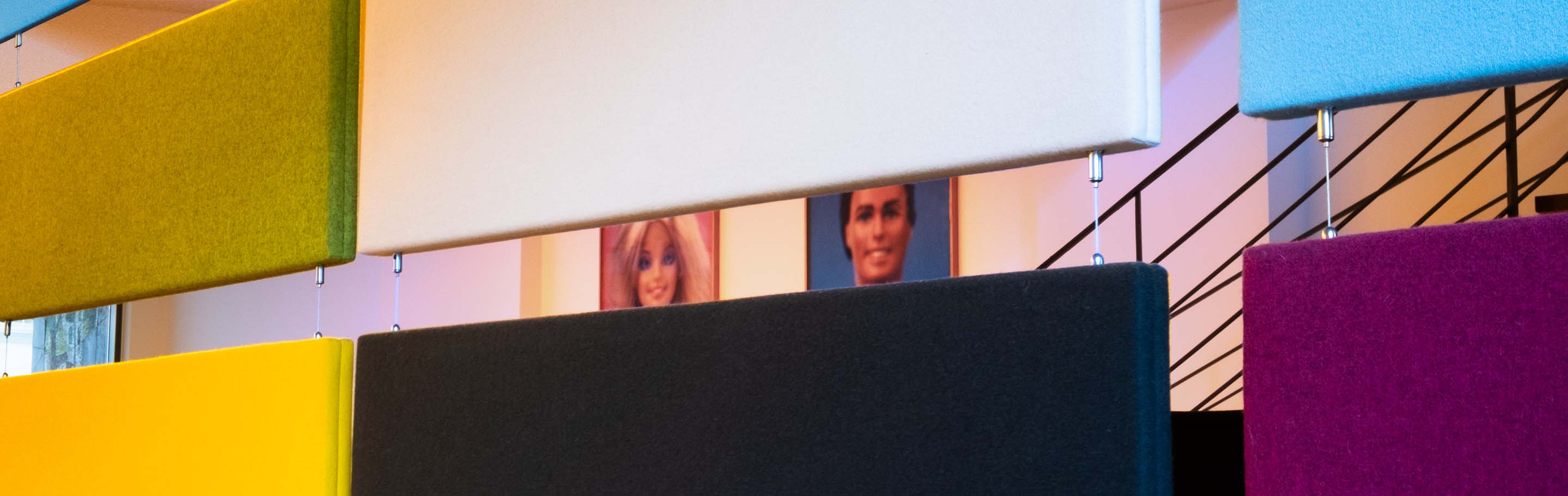View through colorful hanging textile panels, in the background you can see excerpts from posters with Barbie and Ken