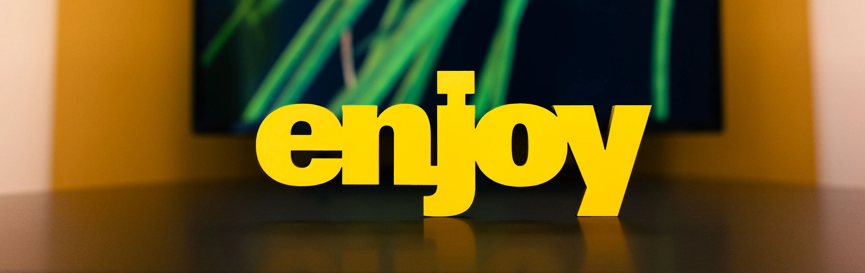 A yellow stand-up display with the word "Enjoy" against a blurred background from the agency premises