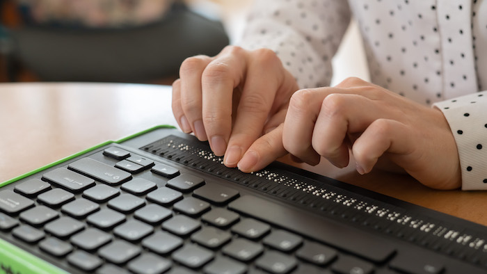 Hands of a person using a computer keyboard and braille display